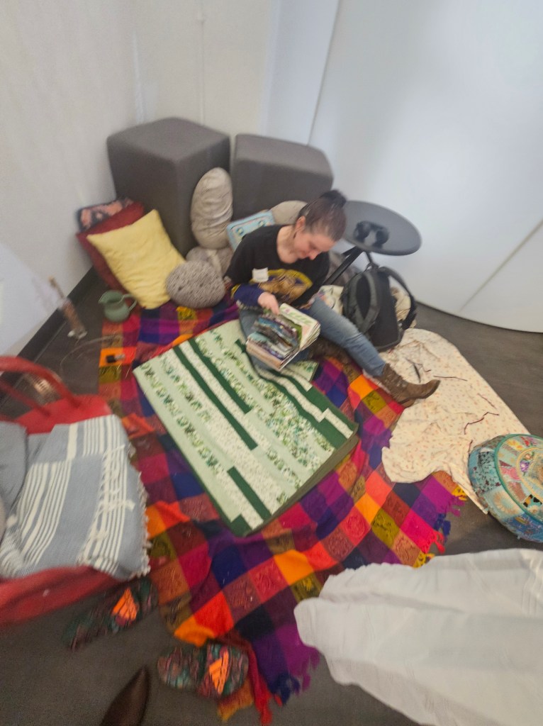 a photo of a woman seated in the "Cozy Space" of Sensory Interruptions, leafing through an artist book.