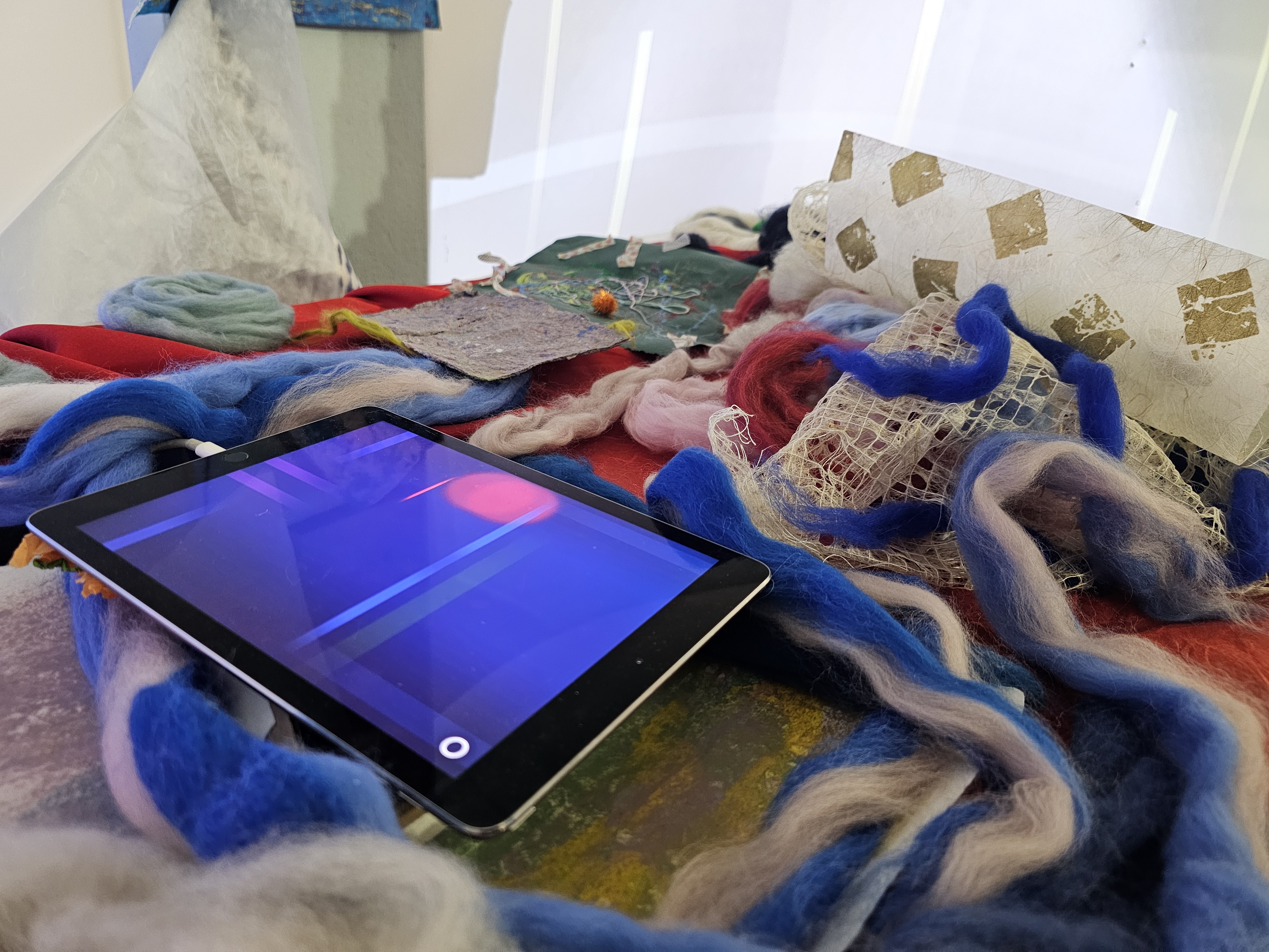 [A photo of the "co-motion" station which contains the generative music app "Bloom" on top of spread out fibers and papers.]